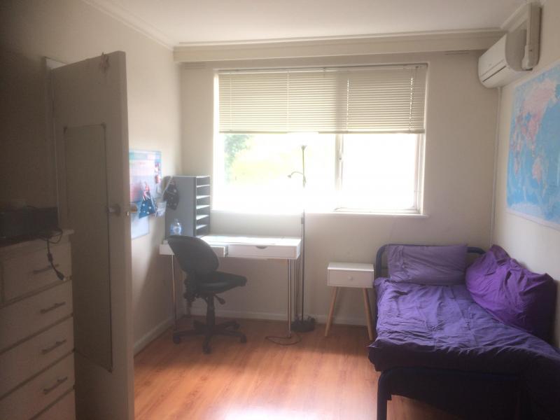 sun filled west facing room with; desk, lamp, bedside table, single bed, air conditioner